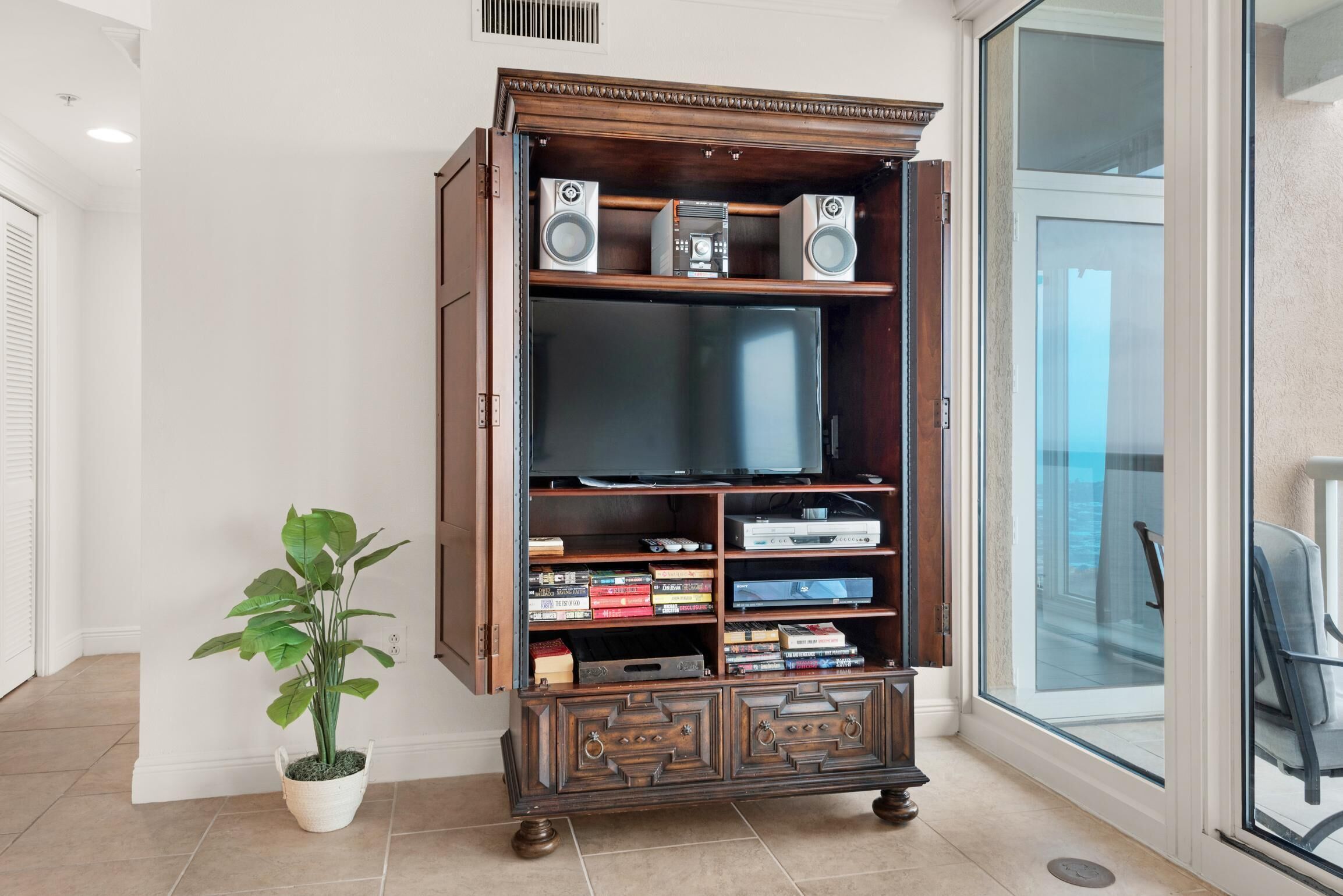 A wooden entertainment center with a flat-screen TV, speakers, and a potted plant.