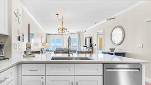 A modern kitchen with white cabinetry, a stainless steel dishwasher, and a large island with a sink. - Emerald Isle Unit 703 (Pensacola Beach)