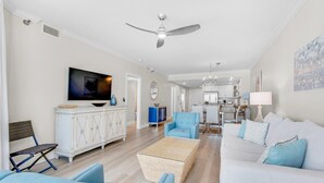 A spacious living room with a ceiling fan, a television, and a dining area in the background. - Emerald Isle Unit 703 (Pensacola Beach)