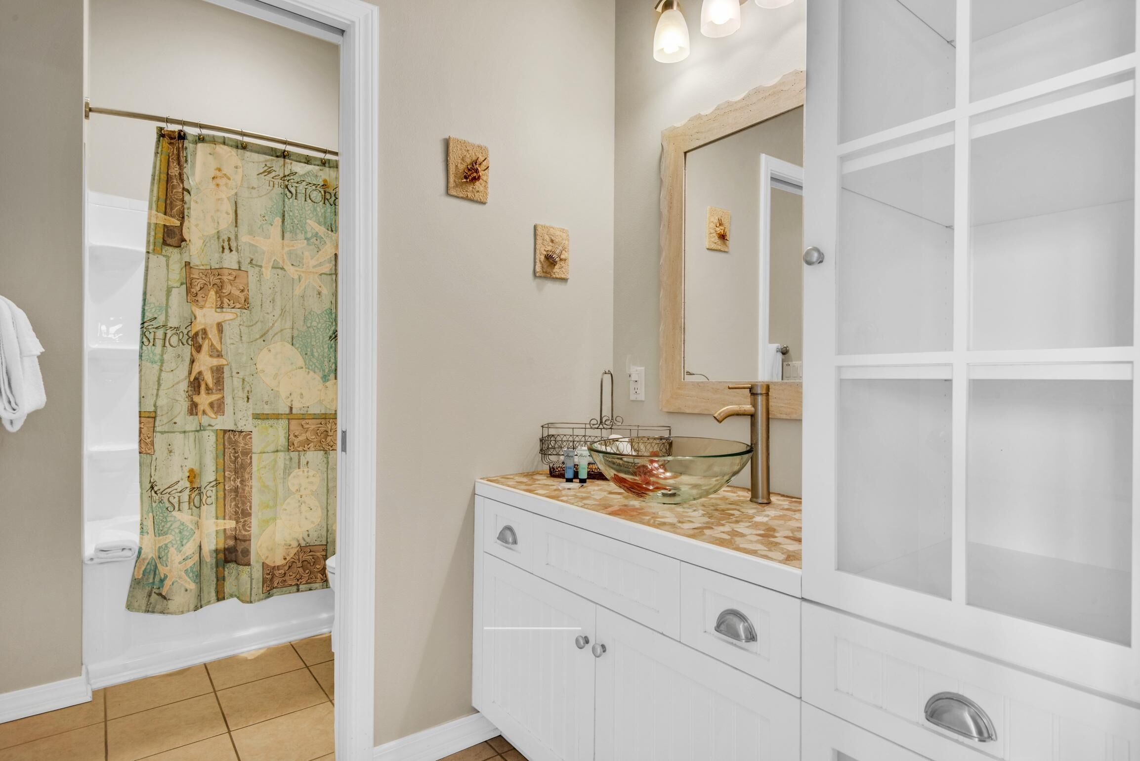Un baño con cortina de ducha, un lavabo con un recipiente de vidrio y un espejo.