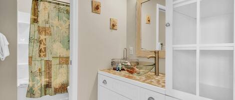 Un baño con cortina de ducha, un lavabo con un recipiente de vidrio y un espejo.