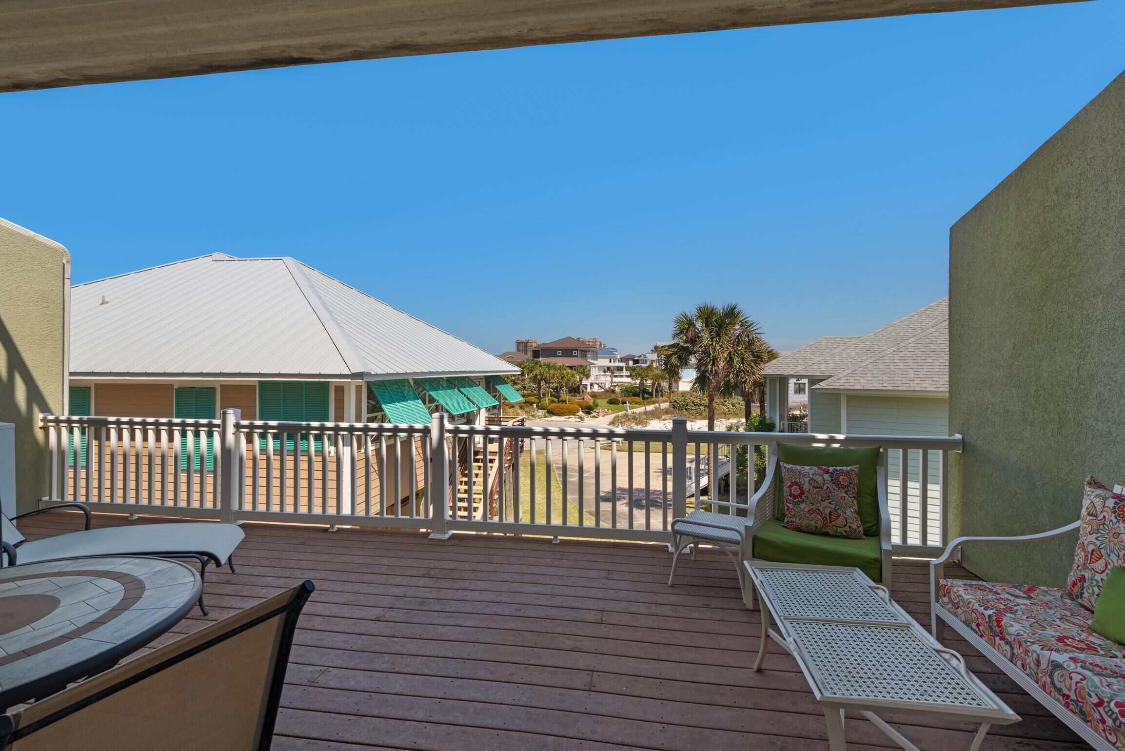 Um deck de madeira com área de estar externa, guarda-corpo branco e vista para edifícios ao fundo.