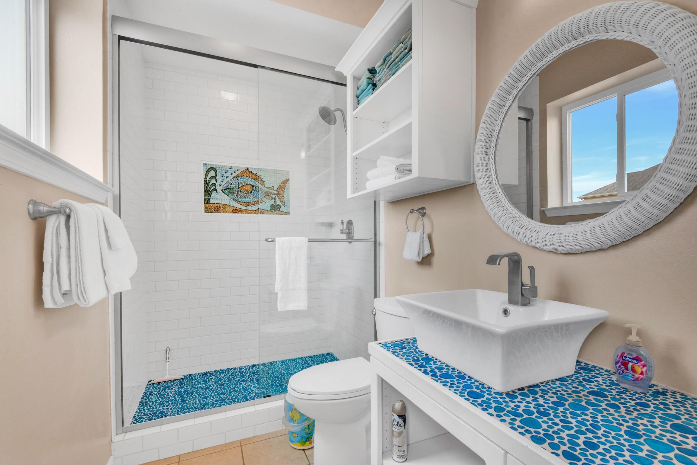 Un baño con ducha envuelta en vidrio, un lavamanos blanco con encimera de mosaico azul y un inodoro blanco.