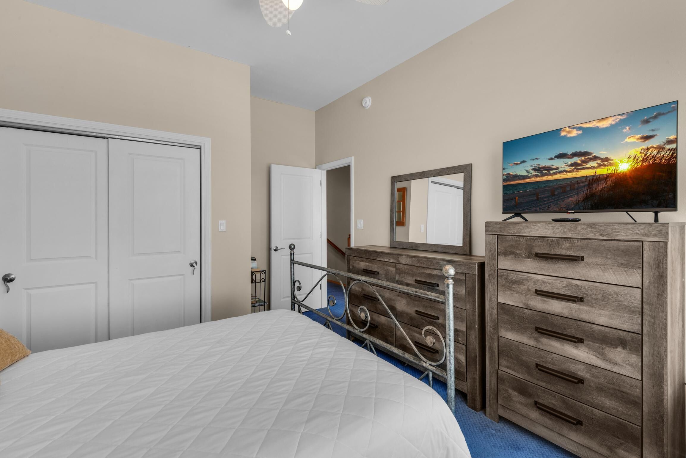 A bedroom with a bed, a dresser, a TV, and a door.