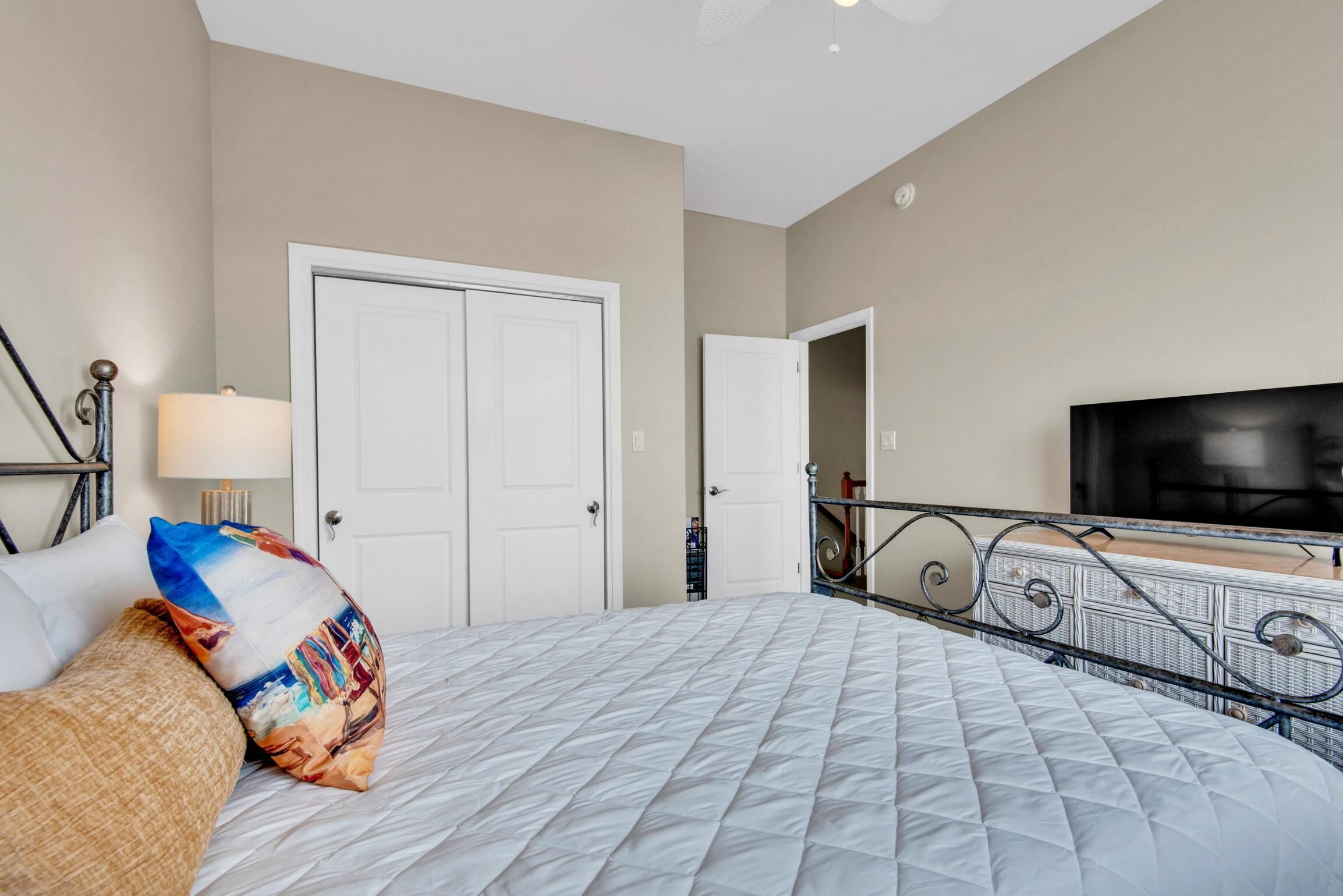 A hotel room with a bed, a TV, a door, and a balcony with a railing.