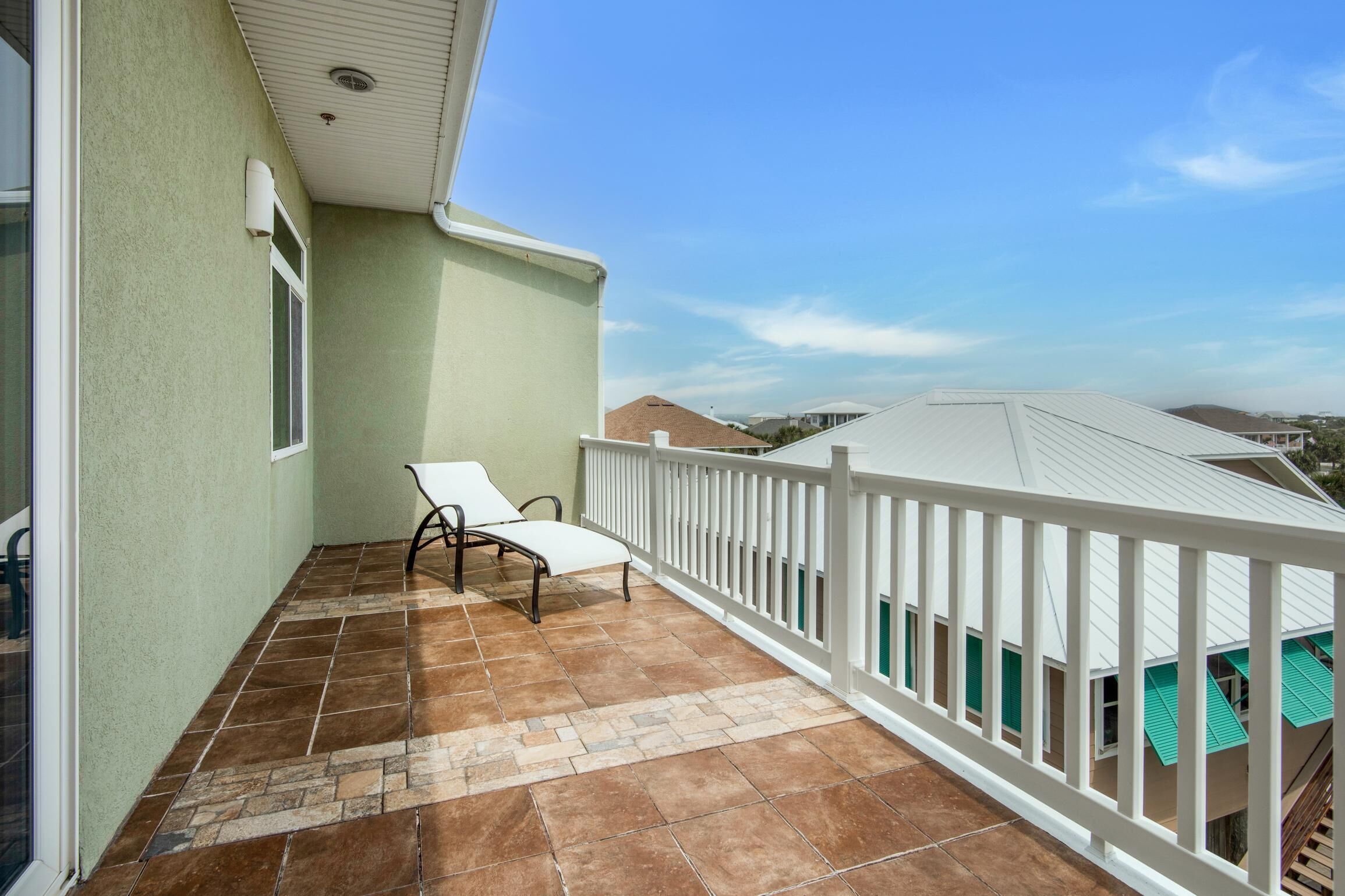 A balcony with a white railing, a pair of white lounge chairs, and a tiled floor.