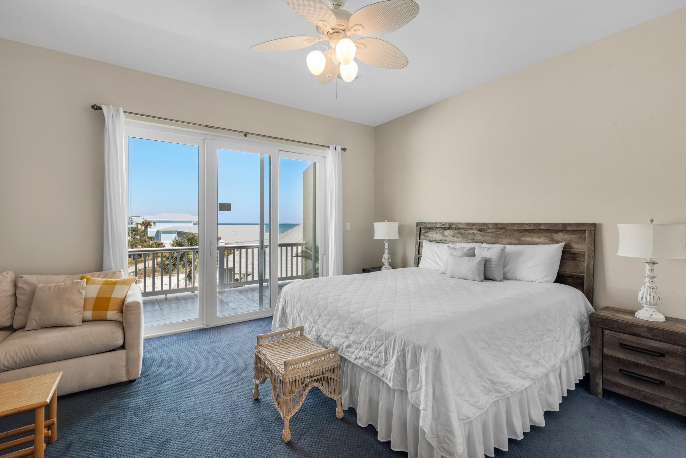 A bedroom with a large bed, a sofa, a small table, and a balcony with a view of the sea.