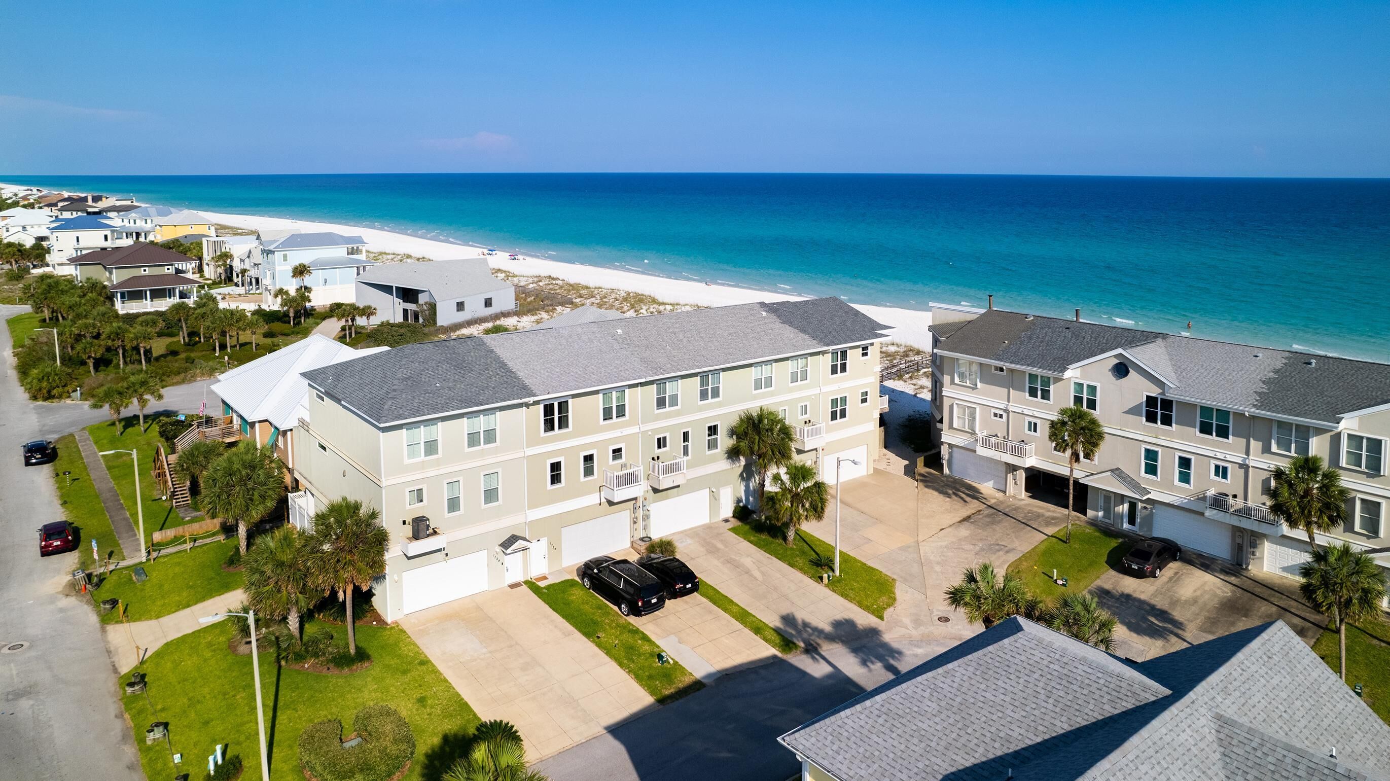 Un quartier résidentiel situé sur la côte, offrant une vue sur la plage, avec des immeubles à plusieurs étages dotés de balcons, un espace de stationnement et un ciel d’un bleu éclatant.