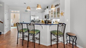 A kitchen with a central island, white cabinets, and hanging pendant lights. - Bonita Bay (Pensacola Beach)