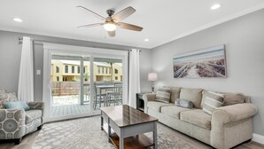 Un salon comprenant un canapé, une table basse, un ventilateur de plafond et une vue sur l’extérieur, visible à travers une porte vitrée.
