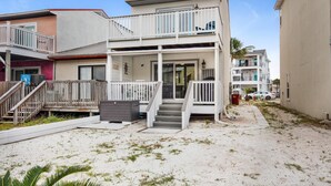 Une propriété de deux étages située en bord de mer, dotée d’un balcon, d’une terrasse couverte et d’un terrain sablonneux.