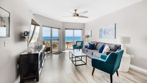 A spacious living room with a view of the ocean, a ceiling fan, and a modern sofa. - Emerald Isle Unit 206 (Pensacola Beach)