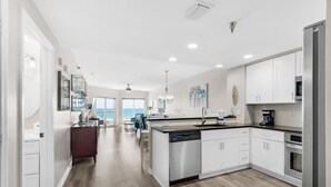 A modern kitchen with white cabinets, stainless steel appliances, and a view to the outside. - Emerald Isle Unit 206 (Pensacola Beach)