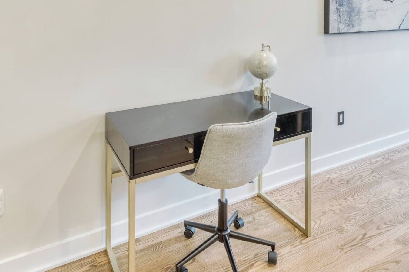 A modern desk with a chair, a lamp, and a framed picture on the wall.