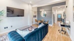 A modern living room with a sofa, a glass coffee table, and a dining area with chairs and a table. - Stylish DC Condo| Free Parking | Near Union Market (Washington)