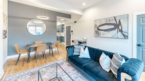 A modern living room with a blue sofa, a dining area with a round table, and a kitchen in the background. - Stylish DC Condo| Free Parking | Near Union Market (Washington)
