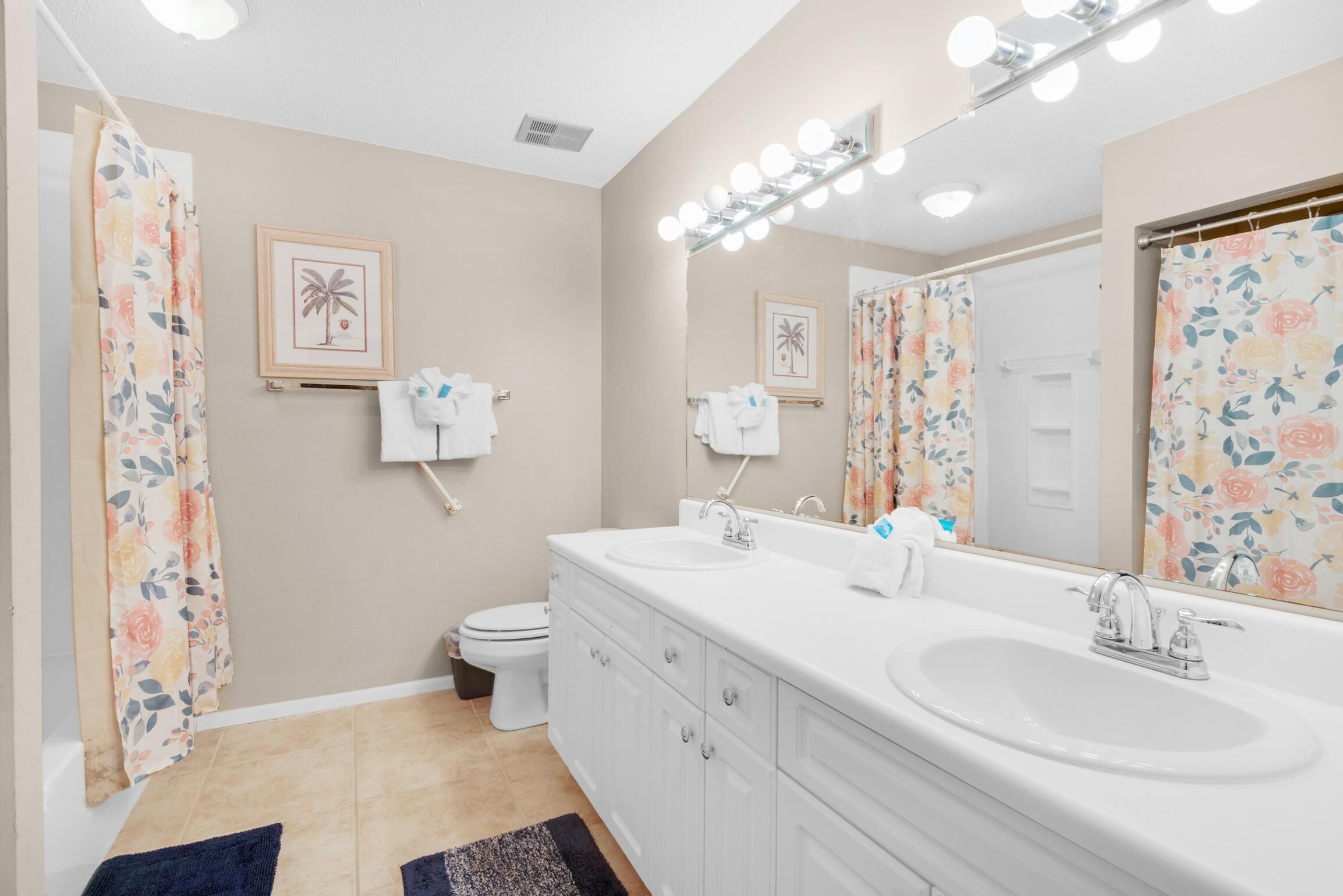 A bathroom with a large mirror, two sinks, and a toilet.