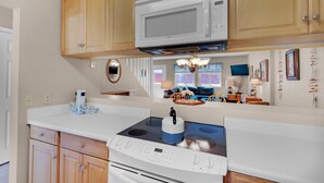 A kitchen with wooden cabinets, a white microwave, a stove, and a countertop with a kettle. - Sugar Beach F-27 (Navarre)
