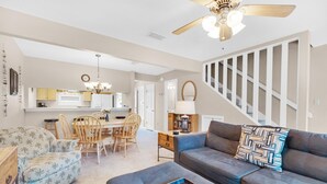 A spacious living room with a sofa, ottoman, and a dining area with chairs and a table. - Sugar Beach F-27 (Navarre)