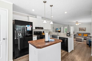 A modern kitchen with a central island, stainless steel appliances, pendant lighting, and a dining area with a gray sofa.