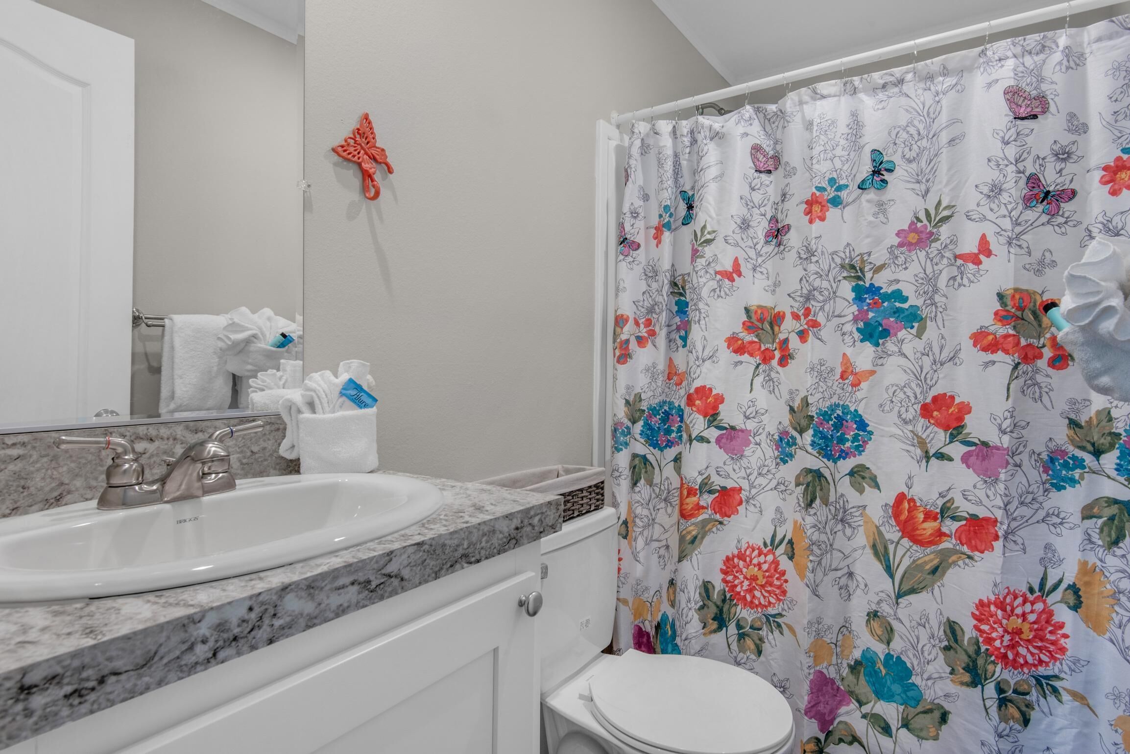 Et badeværelse med en hvid vask, toilet og bruseforhæng med blomstermønster.