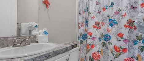 Et badeværelse med en hvid vask, toilet og bruseforhæng med blomstermønster.
