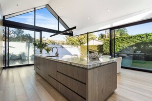 Eine moderne Küche mit einer großen Kochinsel, großen Fenstern und Blick ins Freie.