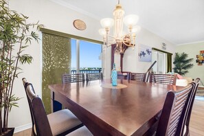 Uma sala de jantar com uma grande mesa de madeira, cadeiras, um lustre e um vaso de planta.