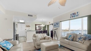 A spacious living room with two beige sofas, a coffee table, and a view of the city through large windows. - South Harbour 4E (Pensacola Beach)