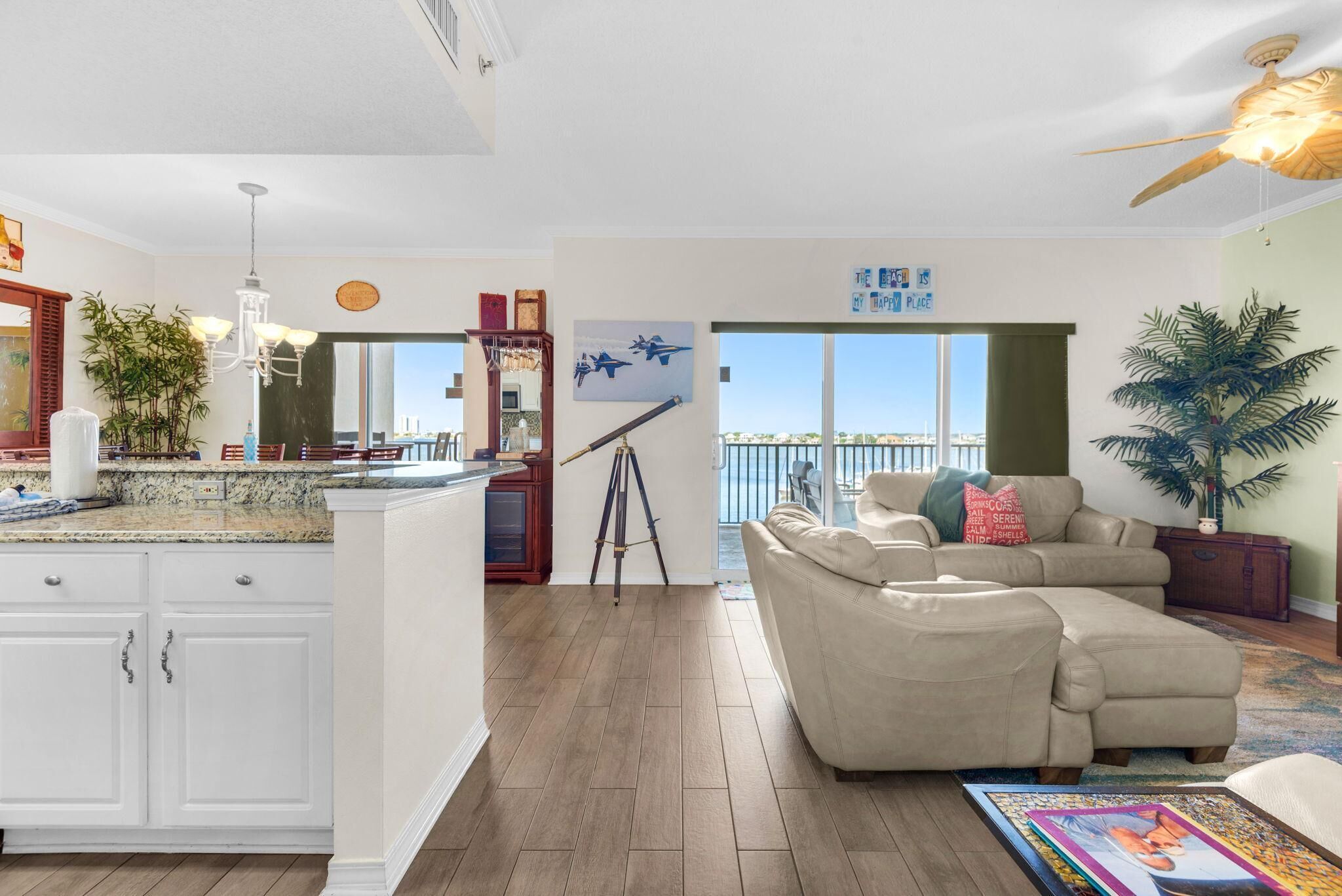 A spacious living area with a large window, a kitchen with white cabinets, a dining area, and a ceiling fan.