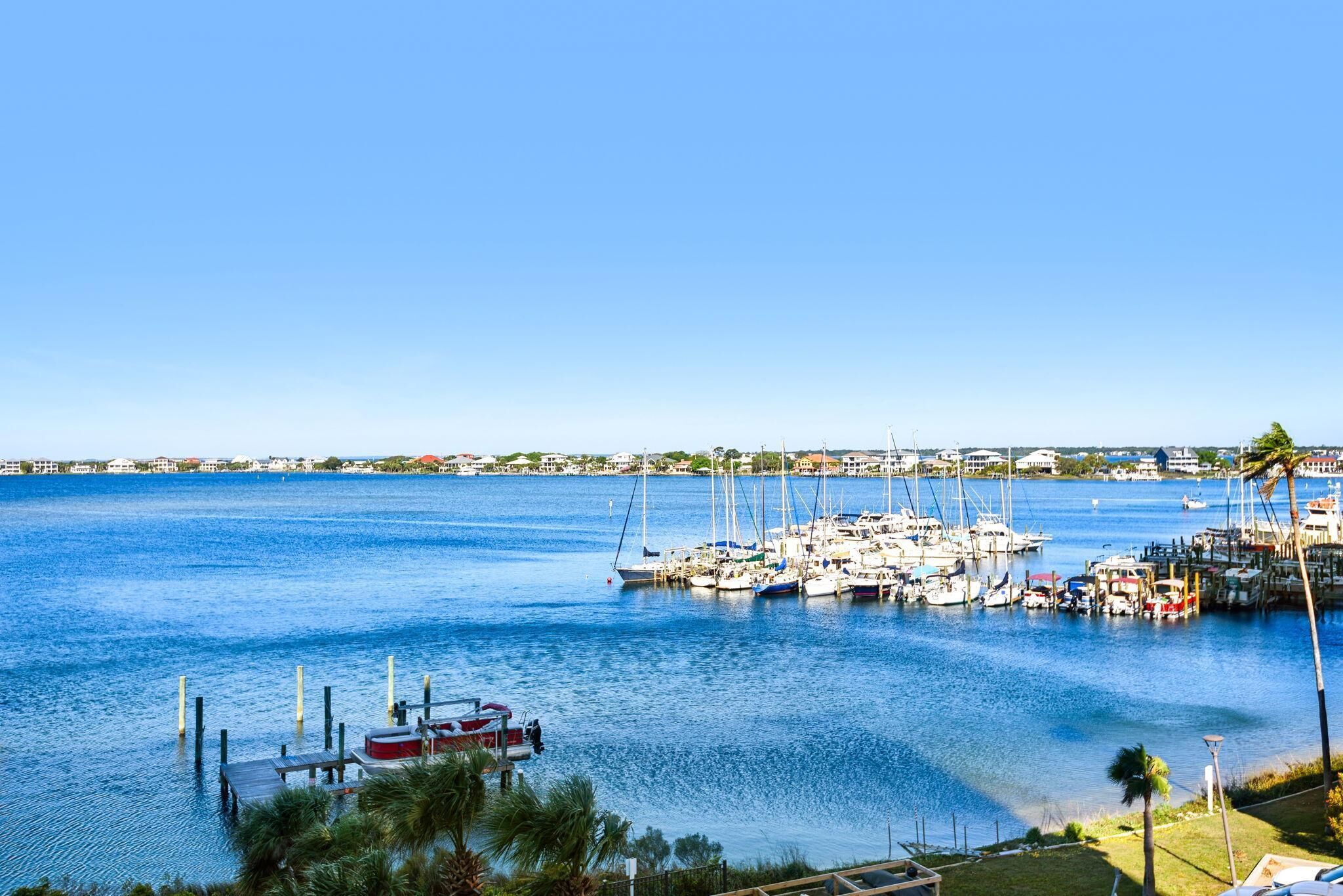 A marina with boats docked, a clear blue sky, and a distant shoreline with buildings.