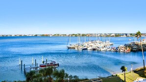 A marina with boats docked, a clear blue sky, and a distant shoreline with buildings. - South Harbour 4E (Pensacola Beach)