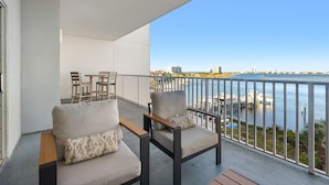 A balcony with two chairs and a table, overlooking a marina with boats and buildings in the distance. - South Harbour 4E (Pensacola Beach)
