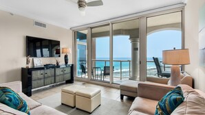 A spacious living room with a large sliding glass door leading to a balcony with a view of the ocean. There is a flat-screen TV mounted on the wall, a sofa, and a coffee table. - Portofino Island Resort 5-1002 (Pensacola Beach)