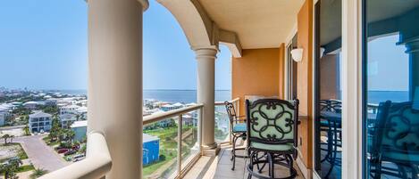 A balcony with a view of the sea and a residential area. There are two chairs and a table.