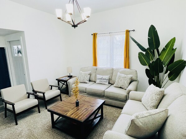 A living room with a sofa, two armchairs, a coffee table, a lamp, and a large plant.