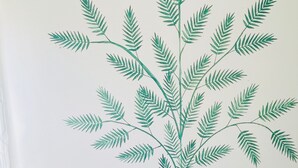 A room with a large wall decal of green fern leaves, a beige armchair, and a carpeted floor.