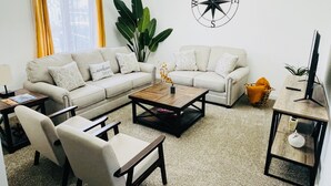 A living room with a sofa, coffee table, chairs, and a television.