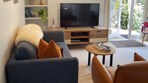 Uma sala de estar moderna com um sofá cinzento, uma poltrona de couro marrom, uma televisão de tela plana e uma luminária pendente.