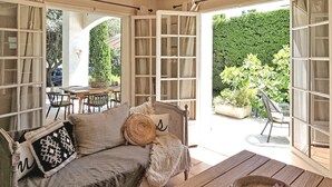 Ein gemütliches Zimmer mit einer Couch, einem Holztisch und Blick auf einen Garten durch offene Türen.