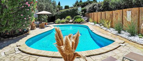 A swimming pool with a curved edge, surrounded by stone tiles and a wooden fence.