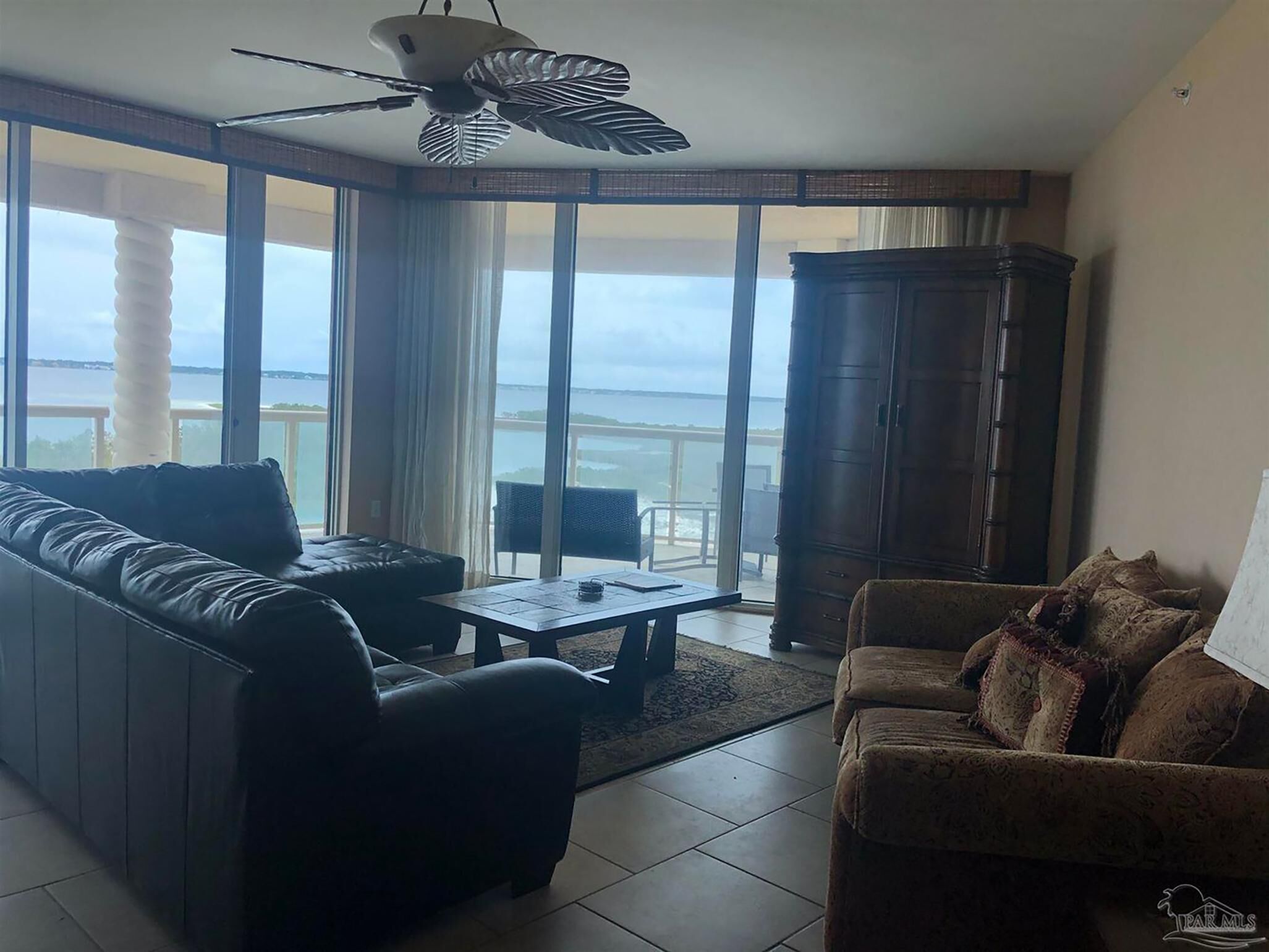 Un salon avec vue sur la mer, un ventilateur de plafond et un grand meuble.