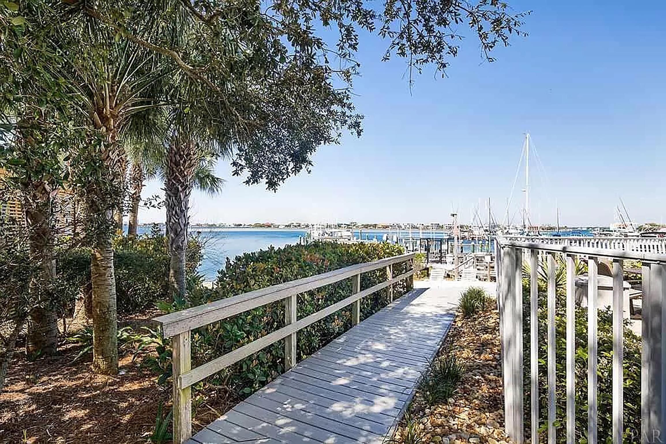 Une promenade en bois qui mène à une marina où sont amarrés des bateaux, et d’où l’on a une vue dégagée sur l’eau.