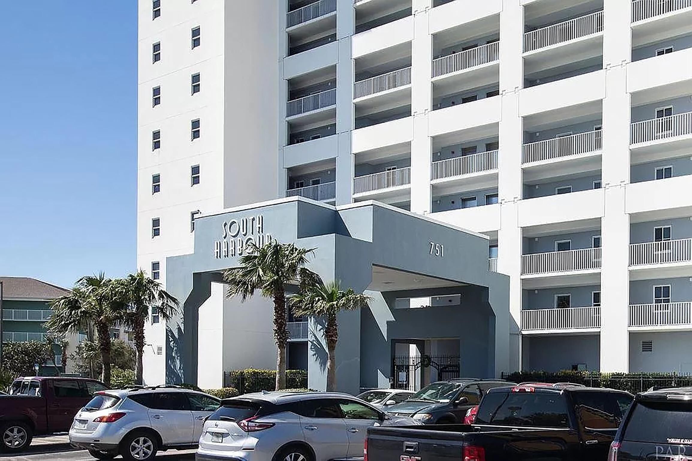 Un hotel de varios pisos con una entrada destacada, balcones y coches estacionados.