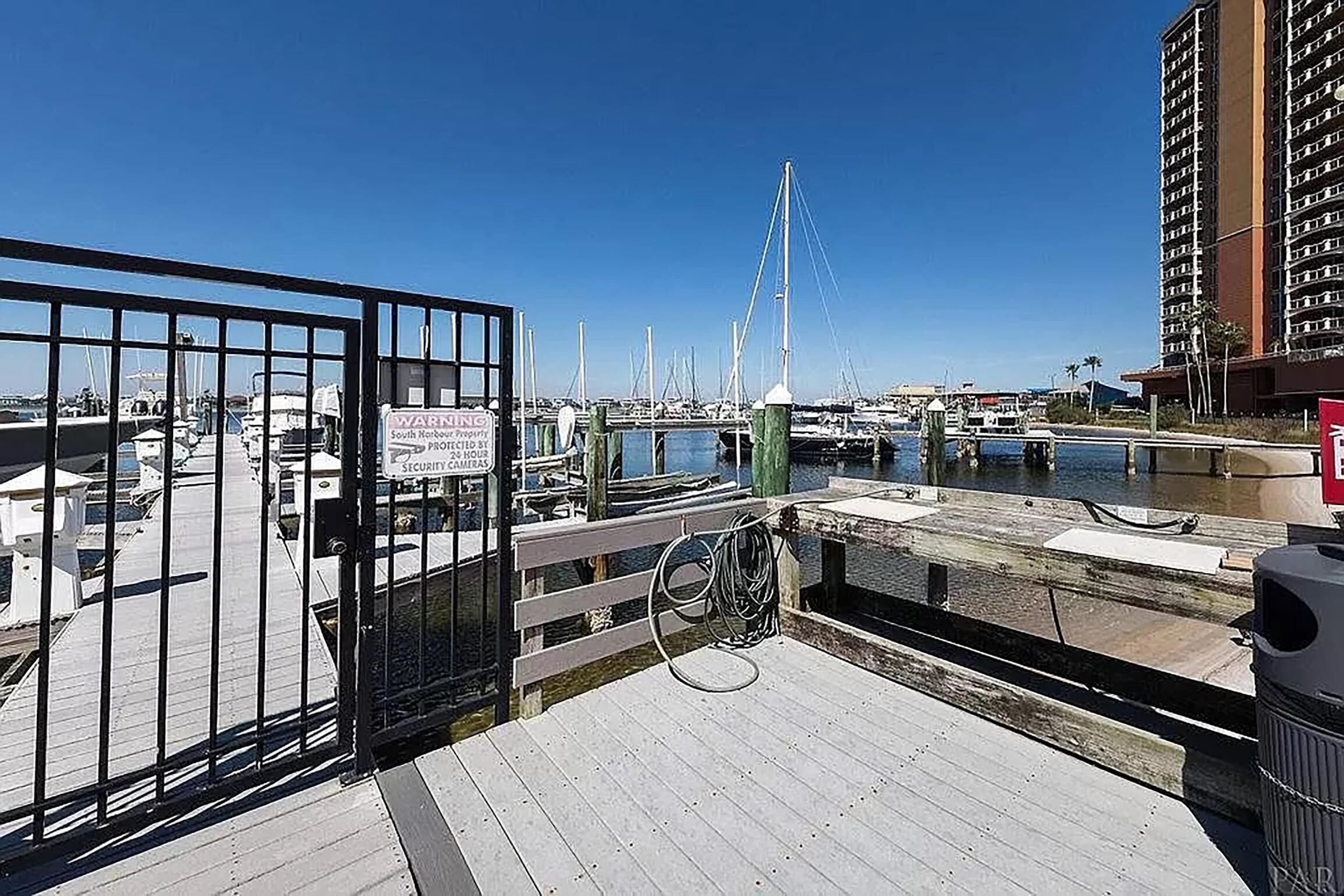 A marina with boats docked, a security camera sign, and a wooden walkway.