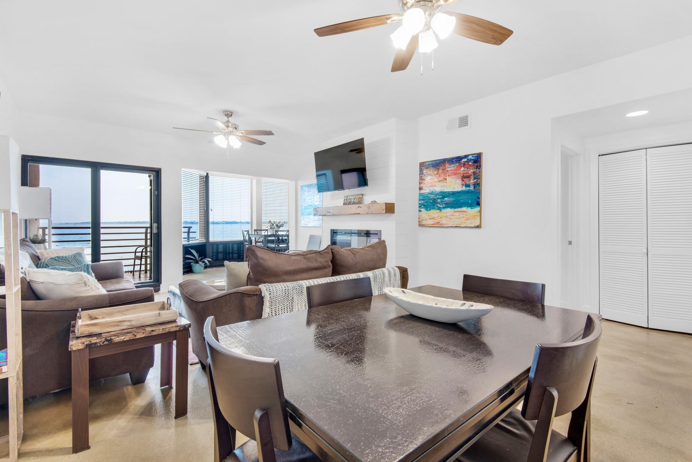 A modern living room with a dark wooden dining table, brown leather sofas, and a ceiling fan.