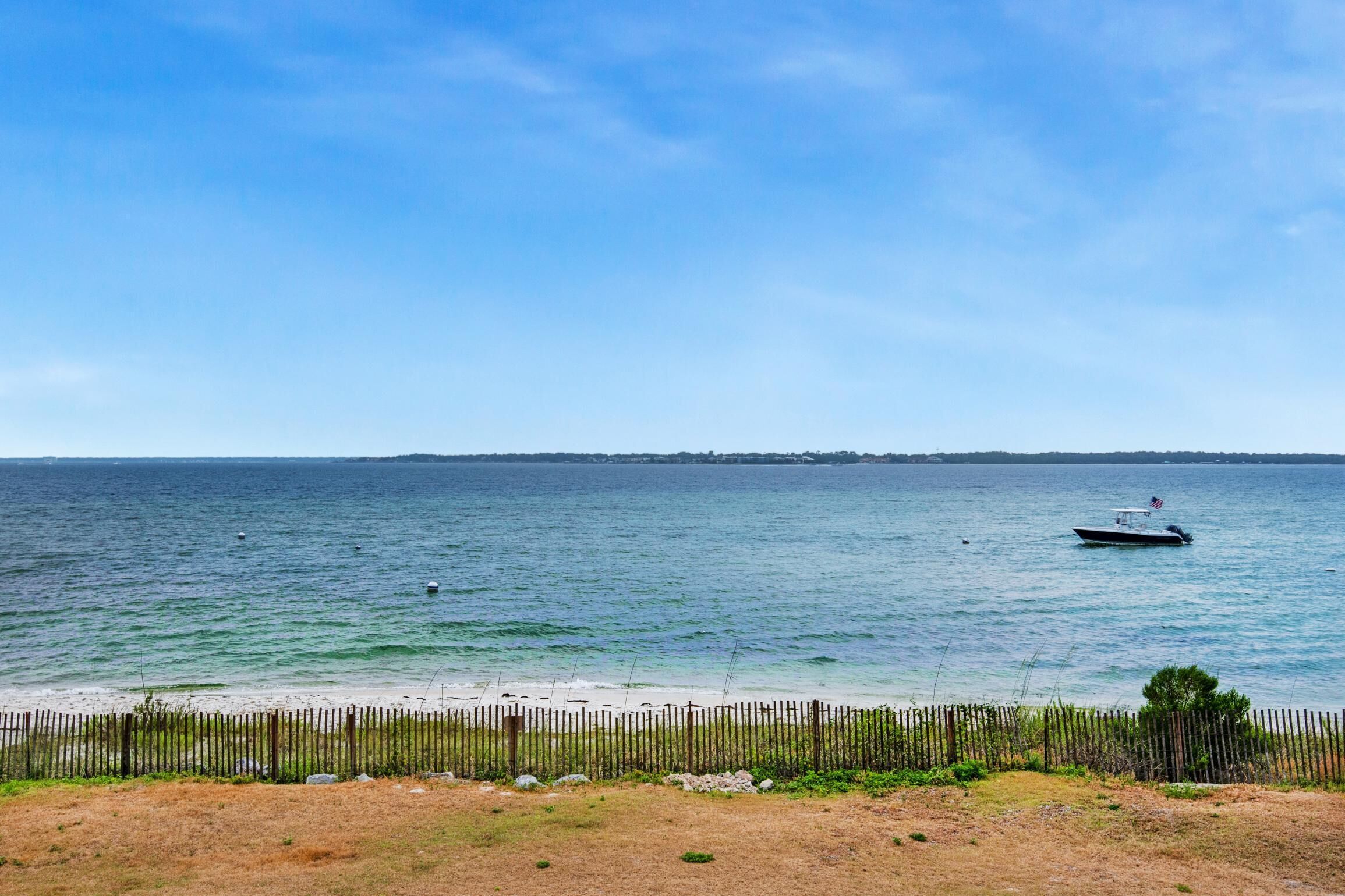 A beach with a wooden fence, a boat on the water, and a distant shoreline.