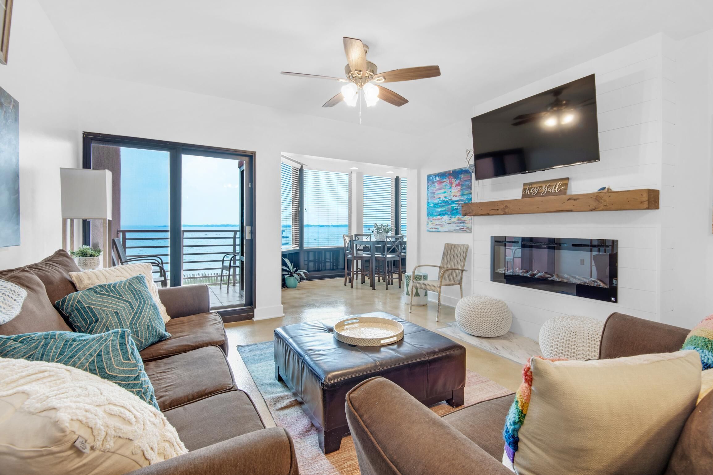 A spacious living room with a large window, a ceiling fan, a flat-screen TV, and a fireplace.