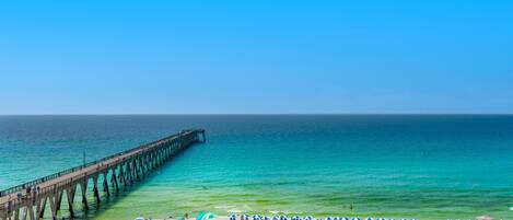 A beach with a pier extending into the ocean, tents, and umbrellas on the sand.