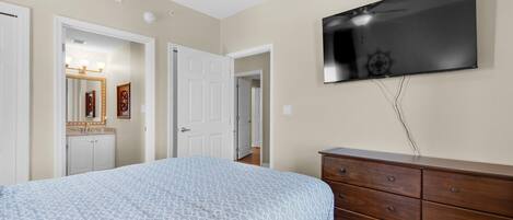 A bedroom with a bed, a dresser, a television, and a door leading to another room.